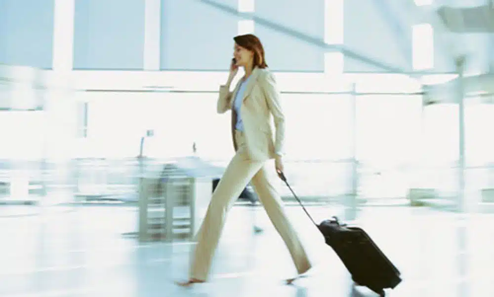 business woman walking through airport on phone with luggage